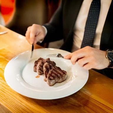 Ein Mann schneidet ein Stück Fleisch auf einem weißen Teller.